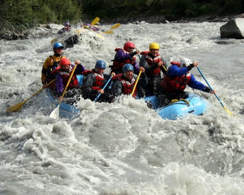 A group of people in a raft splashing through whitewater rapids.