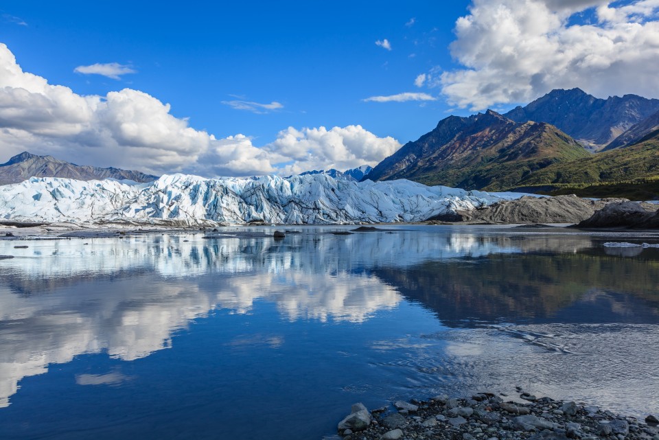 Matanuska Glacier with mountains in the background reflected on the water.