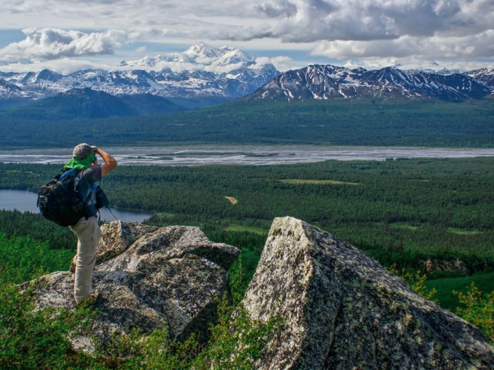 A hike takes a picture of a Alaskan river with mountains in the background.