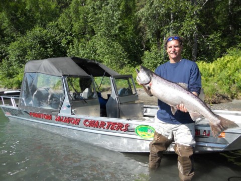A man in waders standing in the water in front of a boat holding a large fish.