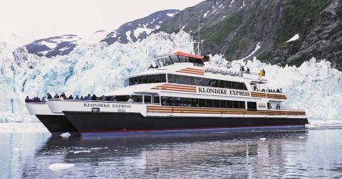 A day cruise ship on the water in front of a glacier.