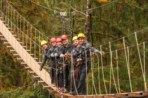 People in ziplining gear walking across a suspension bridge.