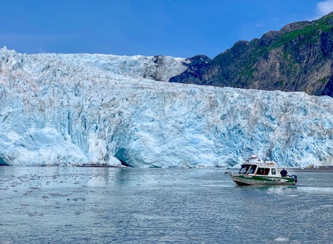 A small sightseeing boat cruises past a glacier.