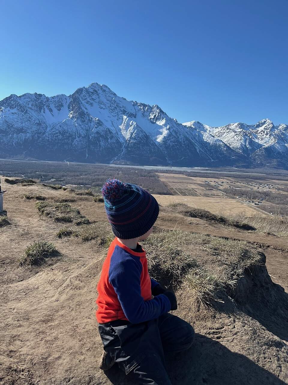 Boy wears a fleece sweatshirt, rain pants and hat on a spring hike
