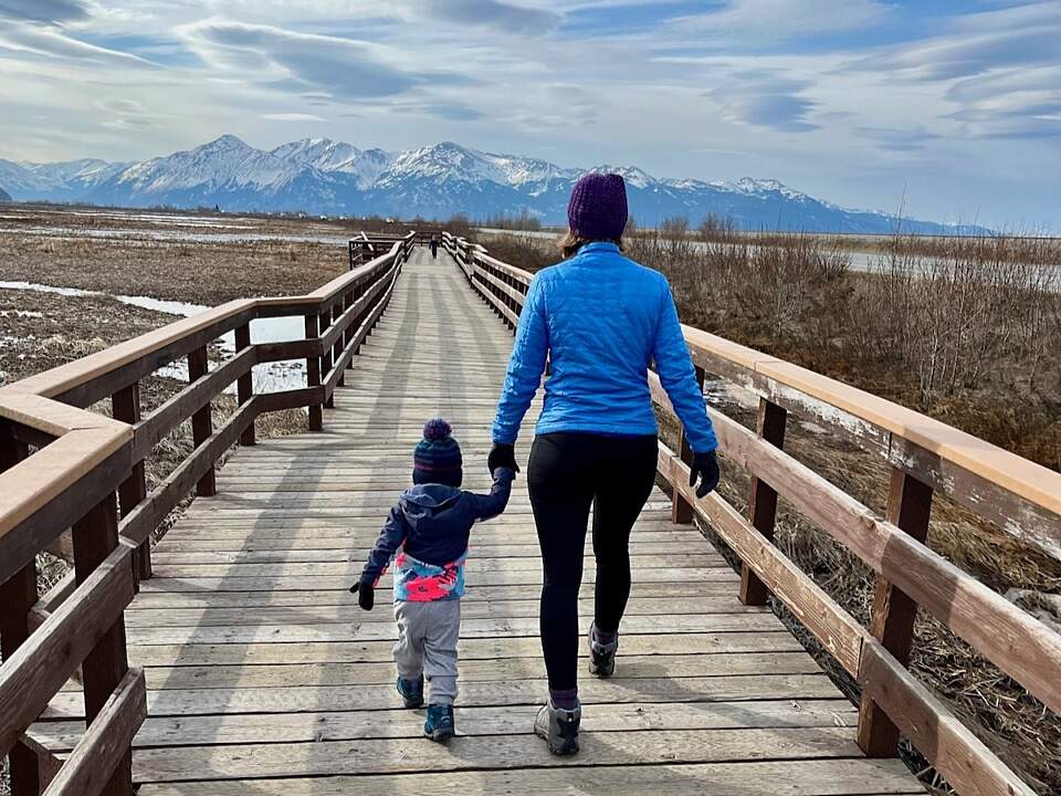 Mother and daughter walk along the boardwalk displaying the concept of layers and wearing a hat.