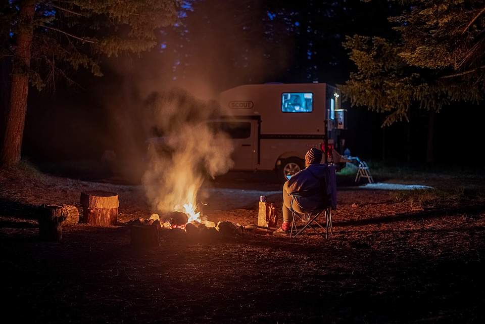 A man sits beside a campfire in Alaska with his rented truck camper