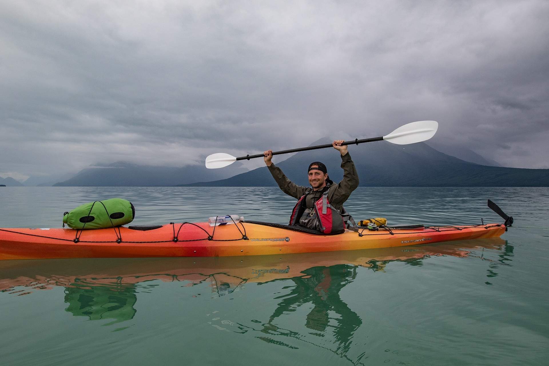Man holds paddle above his head as he kayaks across Lake Clark in Lake Clark National Park