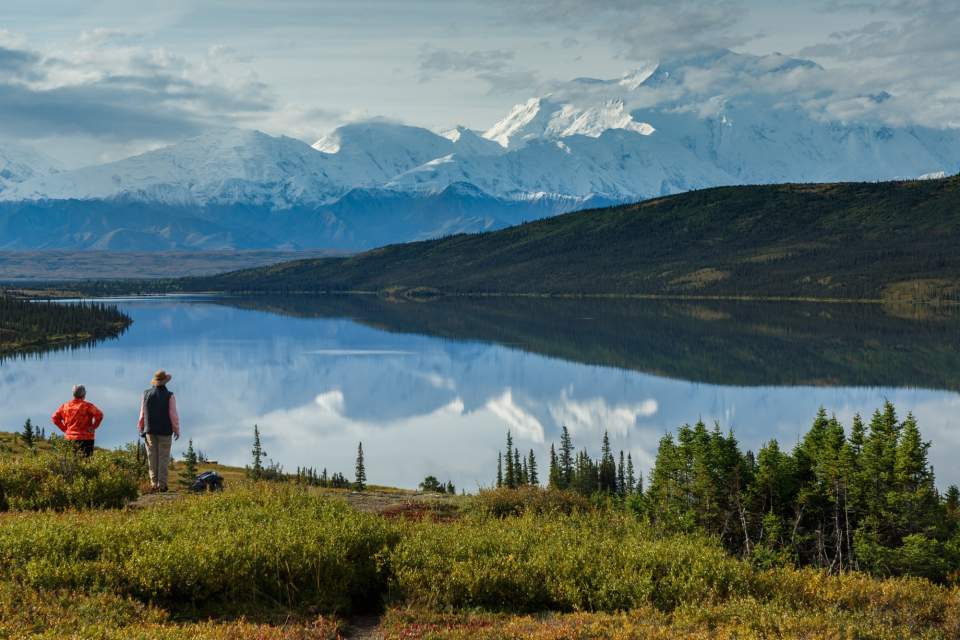 Husband and wife stand in front of Wonder Lake, with Mt. Denali reflecting in the water