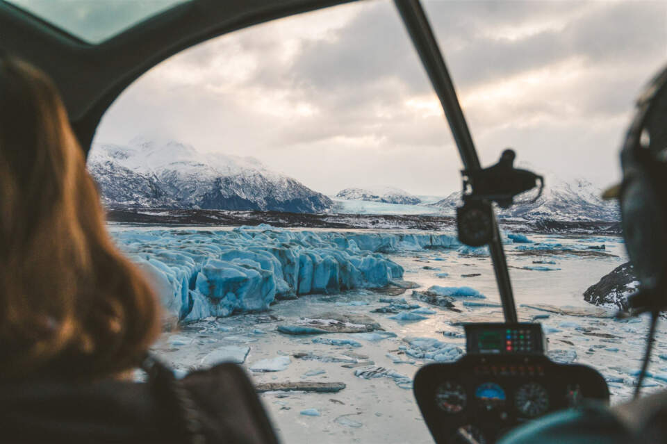 View from inside a helicopter looking out while flying over a glacier