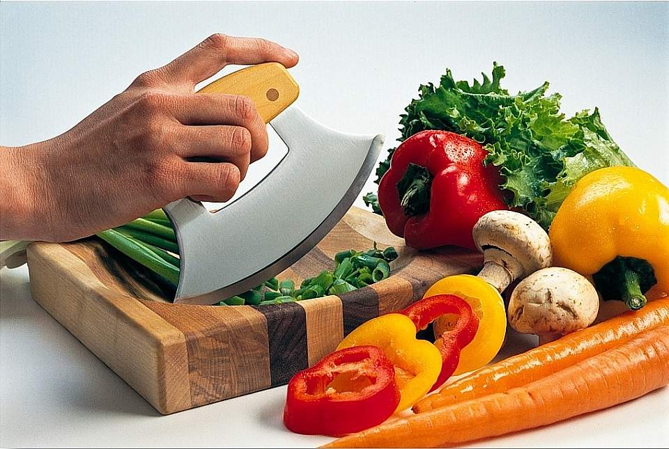 An Ulu knife and cutting board surrounded by fresh vegetables