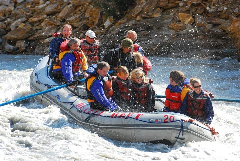 A group of people float down a choppy river on a raft