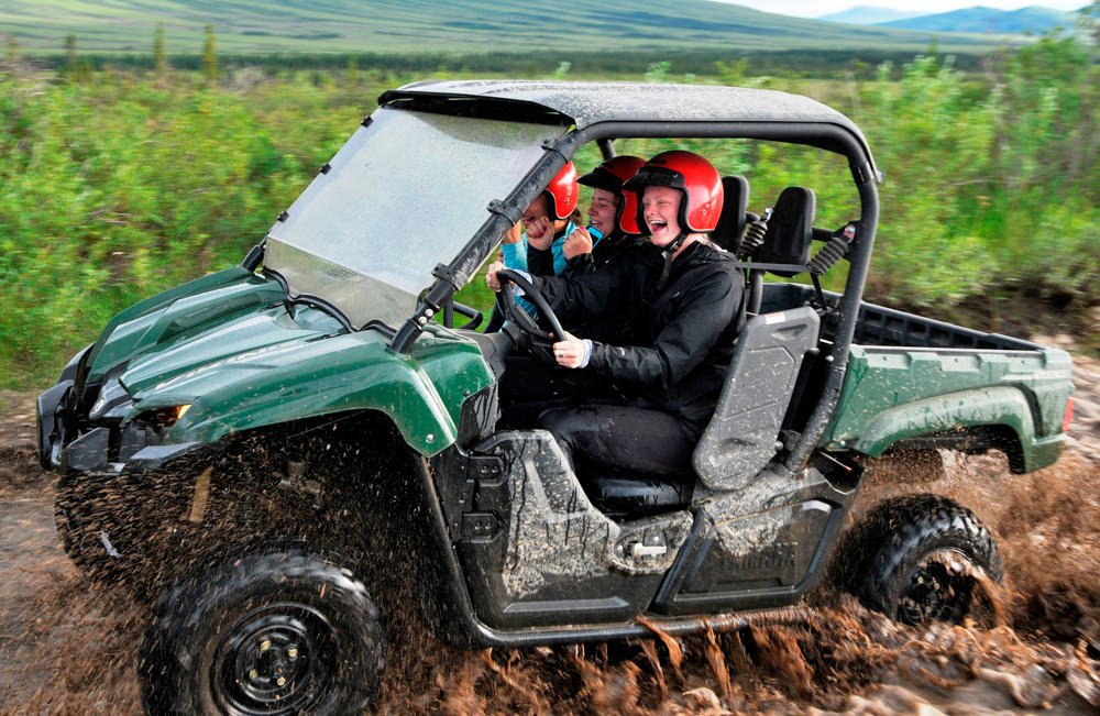 Three people smiling as they splash through the mud on an ATV