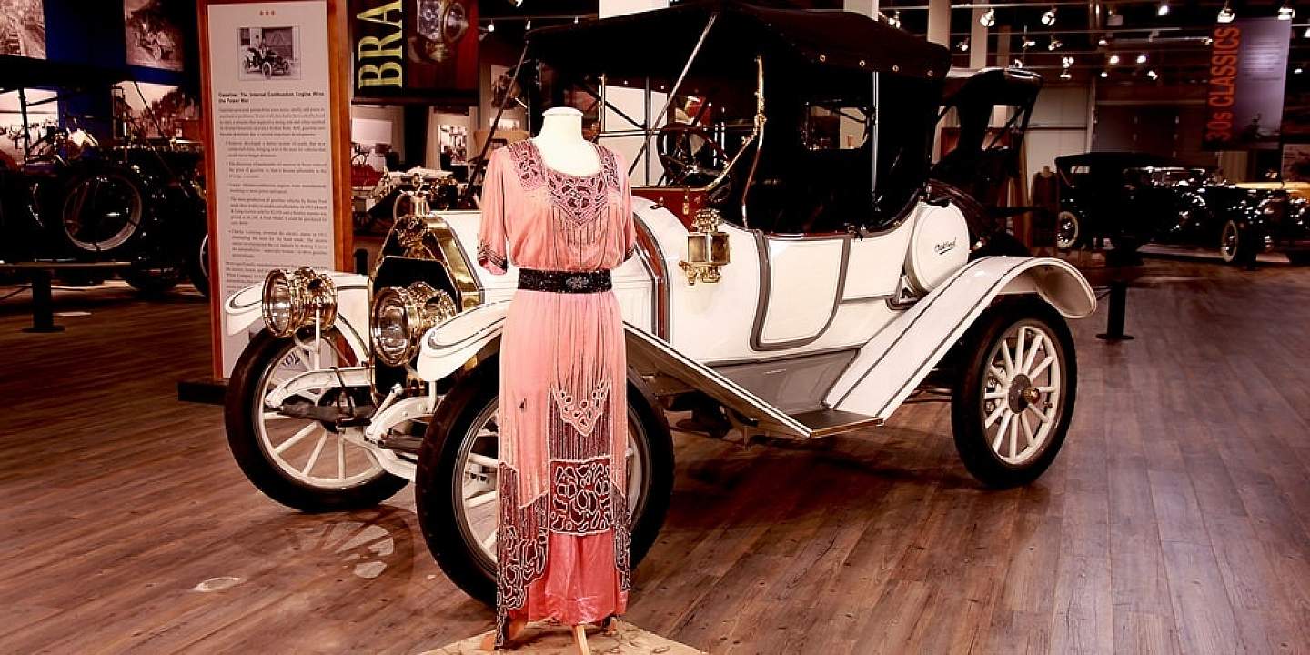 An museum display of a vintage dress and old fashioned car