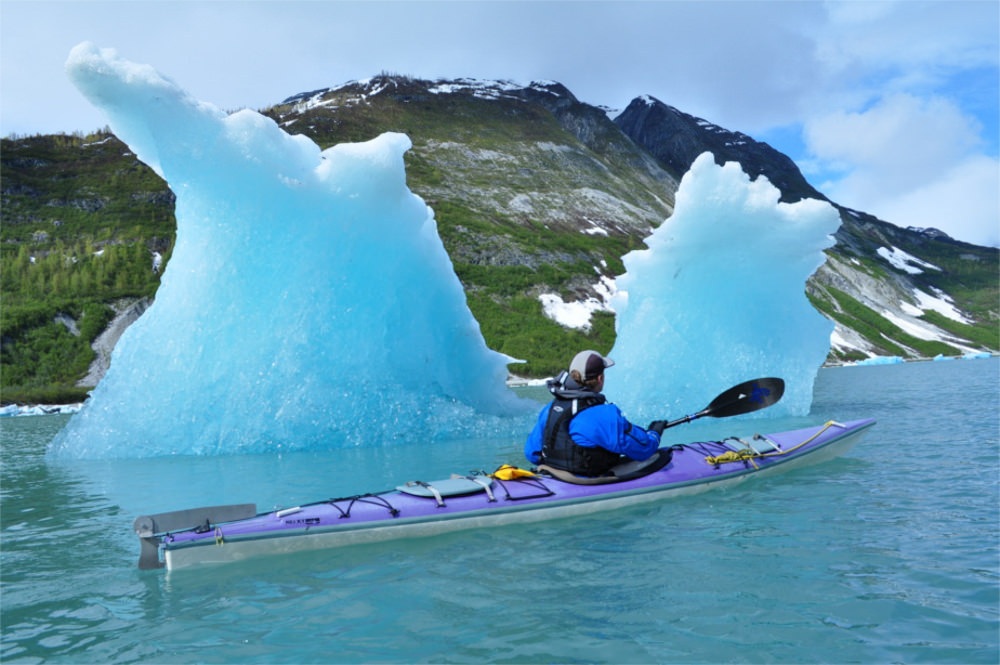 A guest with Alaska Mountain Guides kayaks past an ice berg.