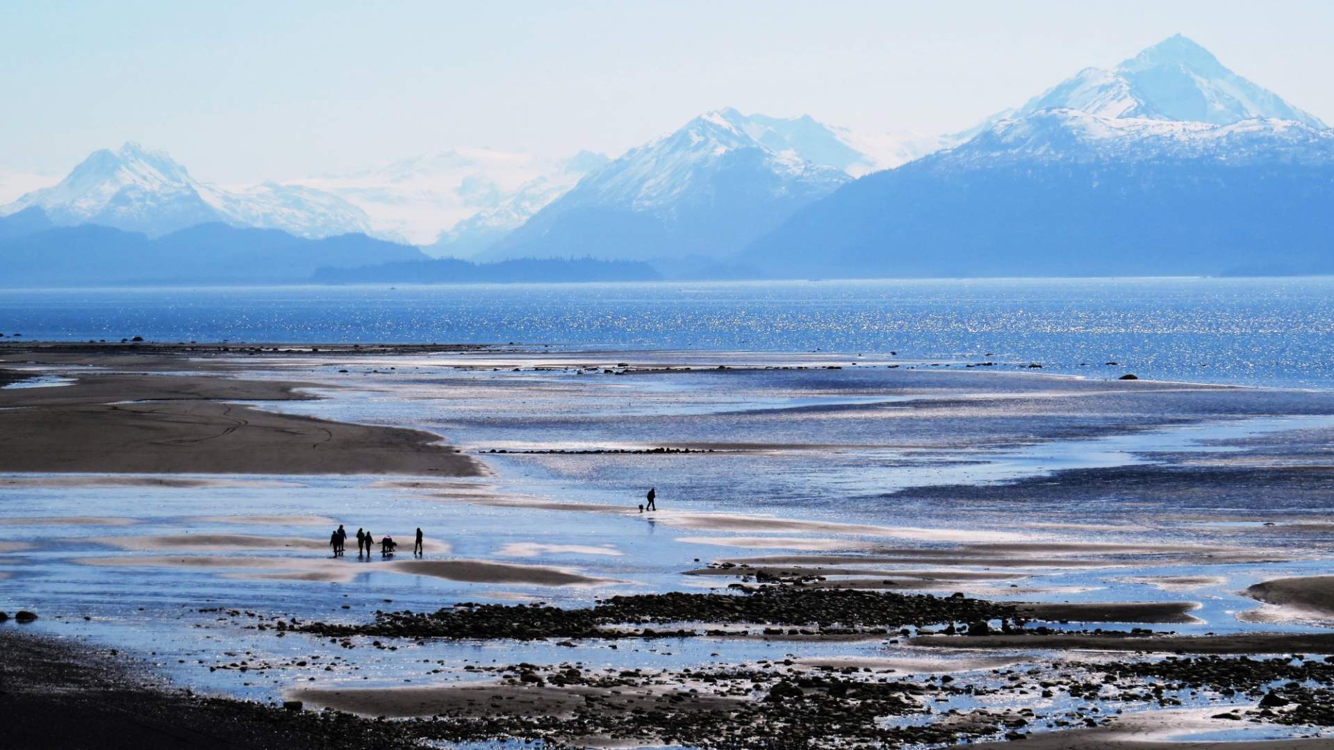 A few people stroll along Bishop's Beach with mountains in the background.