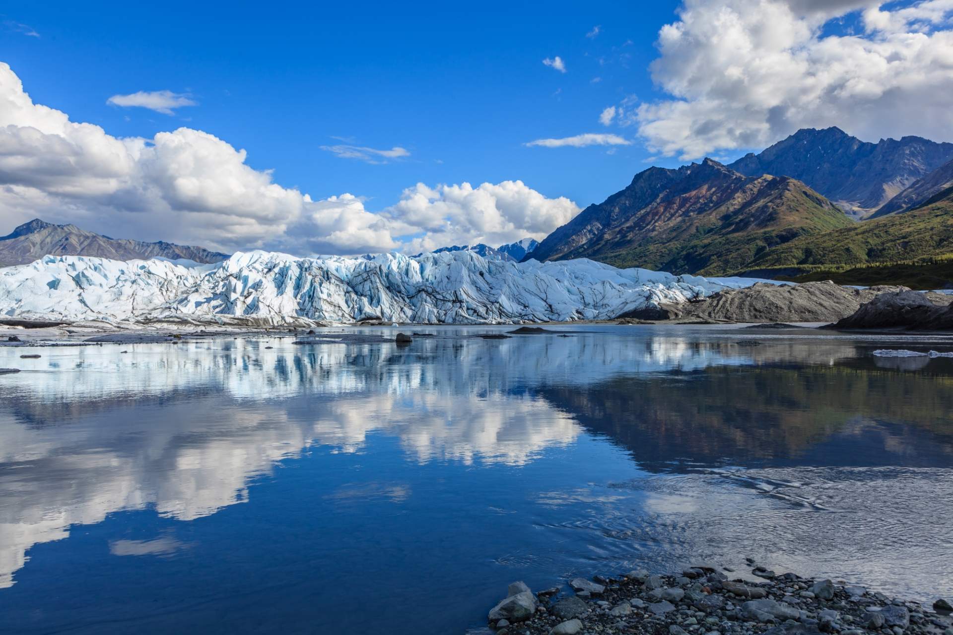 Matanuska Glacier with mountains in the background reflected on the water.