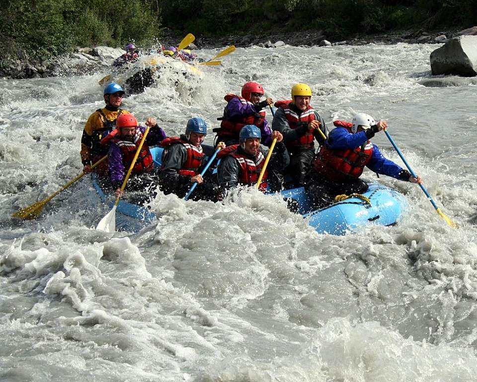A group of people in a raft splashing through whitewater rapids.