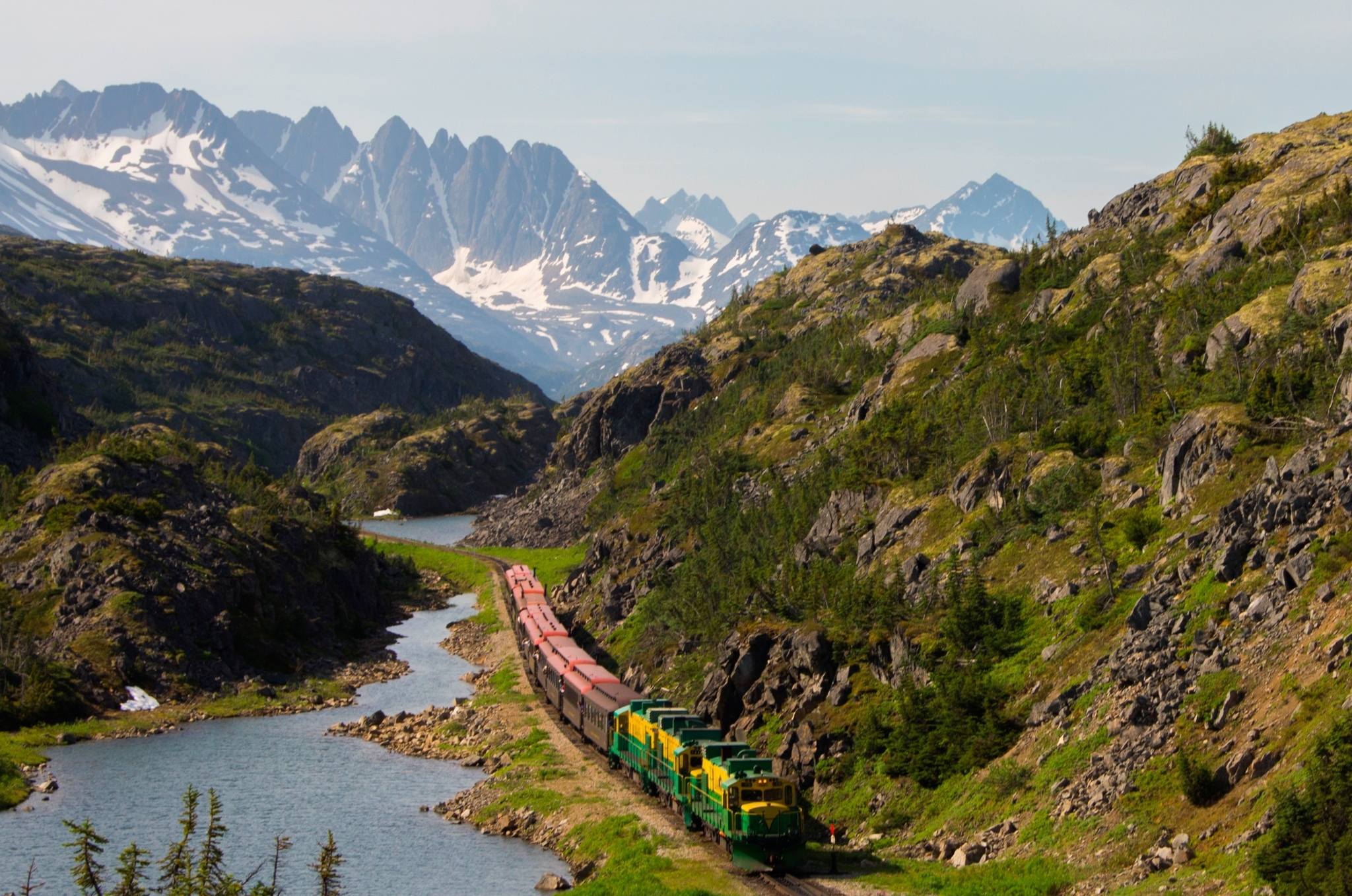 The train moving along the White Pass & Yukon Route surrounded by Alaska mountains and steams