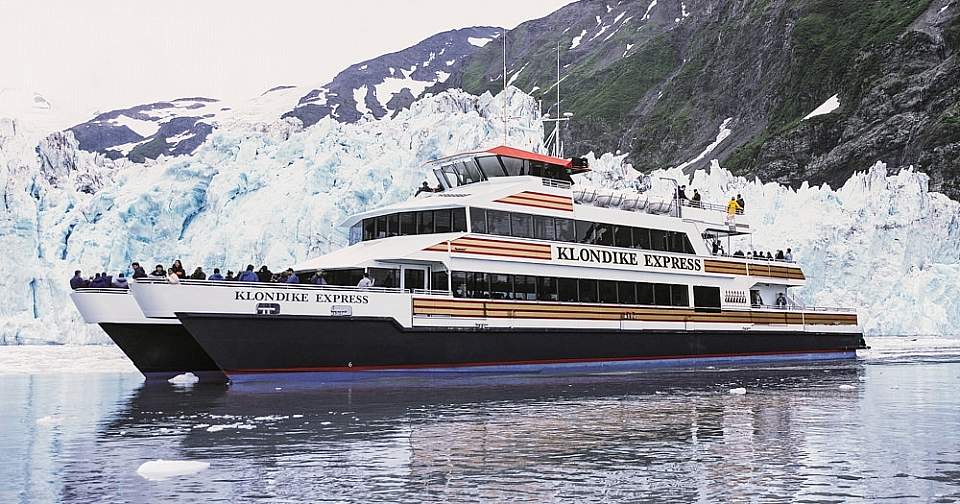 A day cruise ship on the water in front of a glacier.