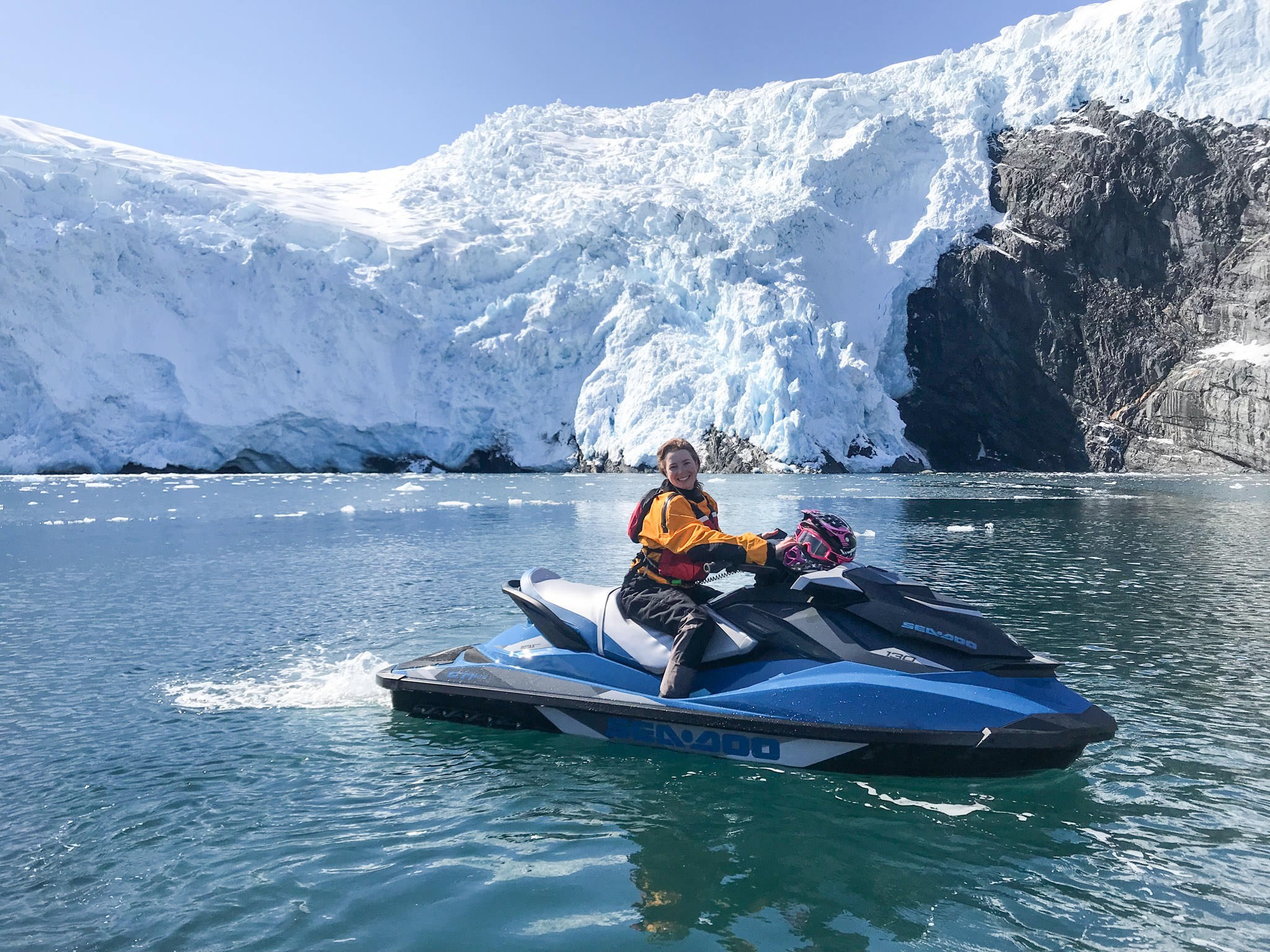 A smiling woman on a jet ski in front of a glacier.