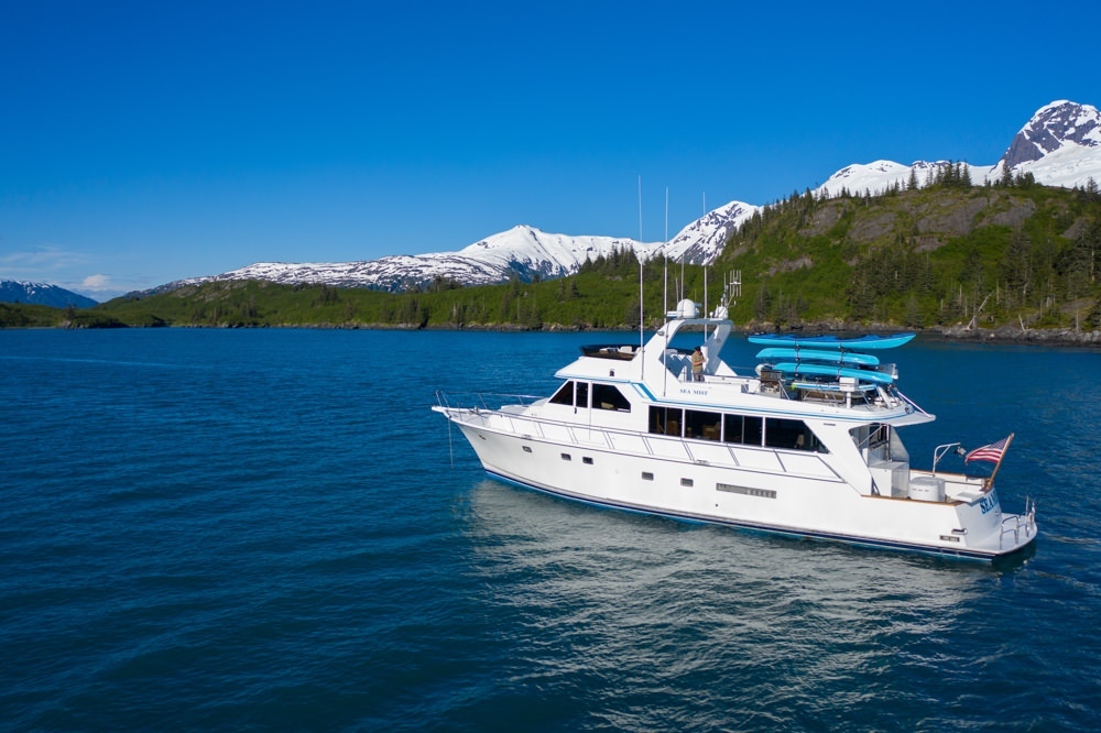 A luxury yacht sails along Prince William Sound with snow capped mountains in the background.