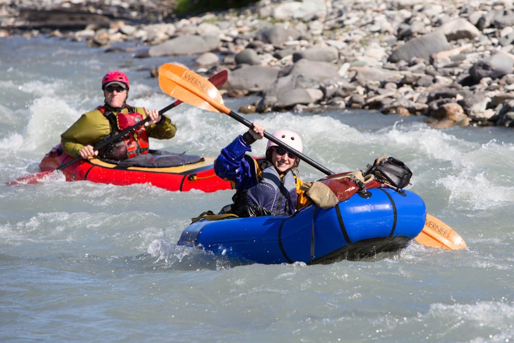 Two people in rafts paddle down a river