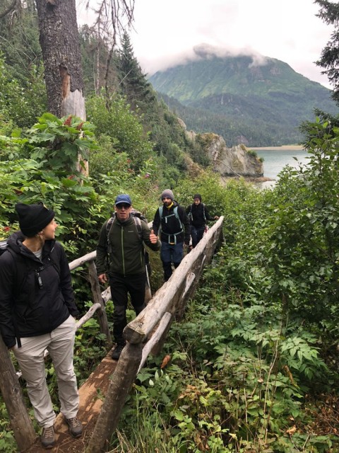 A group of hikers cross a small bridge in a lush environment.