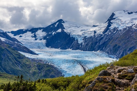 Portage Glacier surrounded by lush greenery and blue mountains.