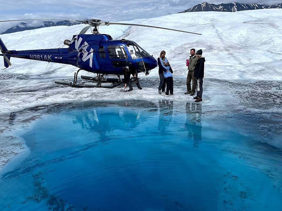 Helicopter lands near a bright blue glacier pool
