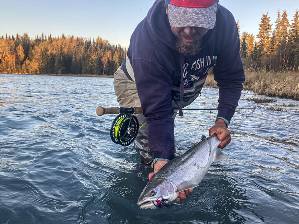 Man holds a fish he caught in the Kenai River close to the water