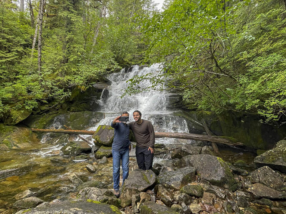 Two women stand in front of a waterfall near Ketchikan for a photo