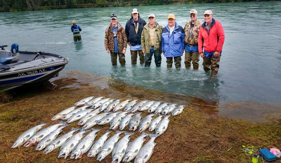 Group of six people in waders stand in water with their fishing haul laid out before them on the beach.