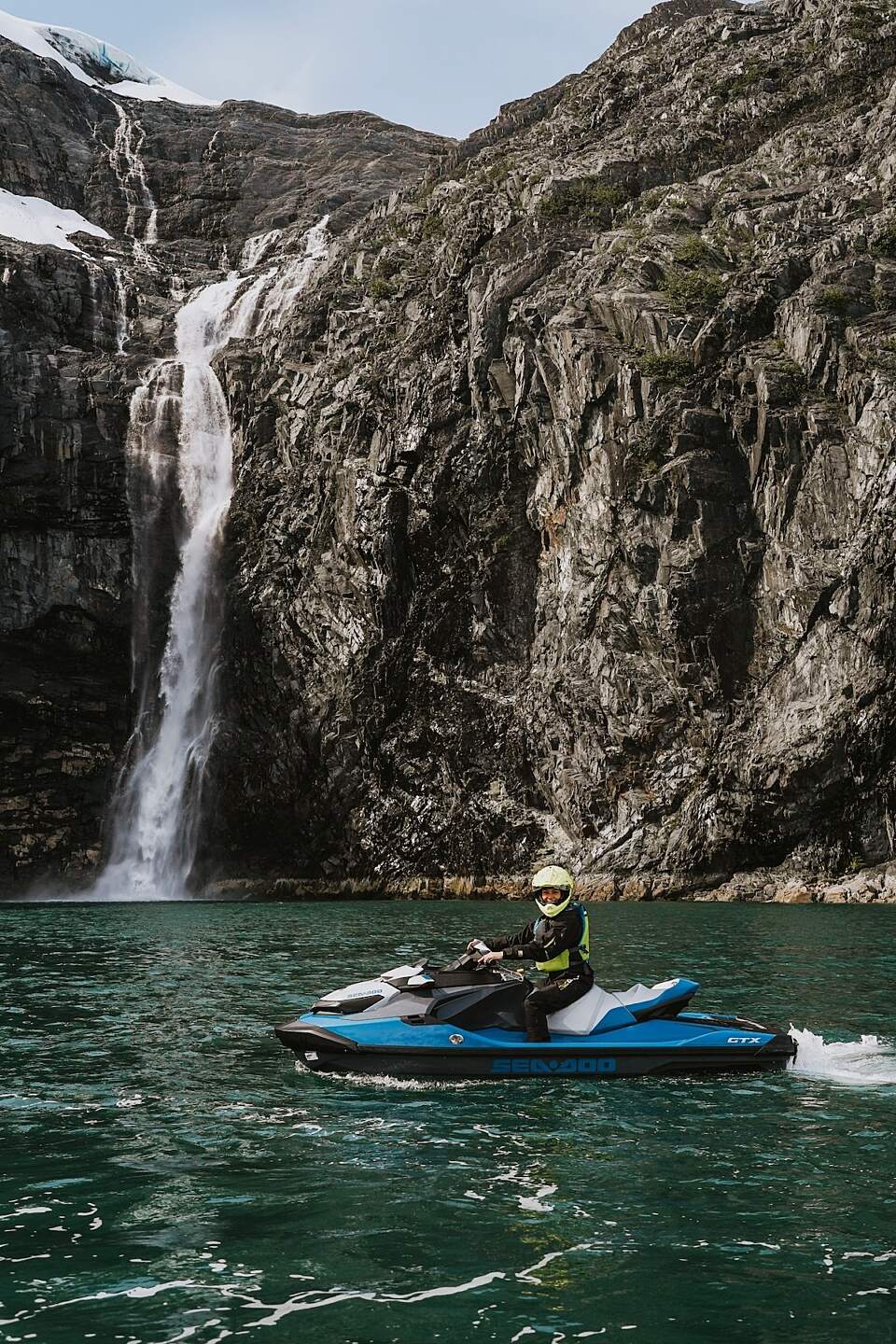A jet skier poses on the water in front of a waterfall