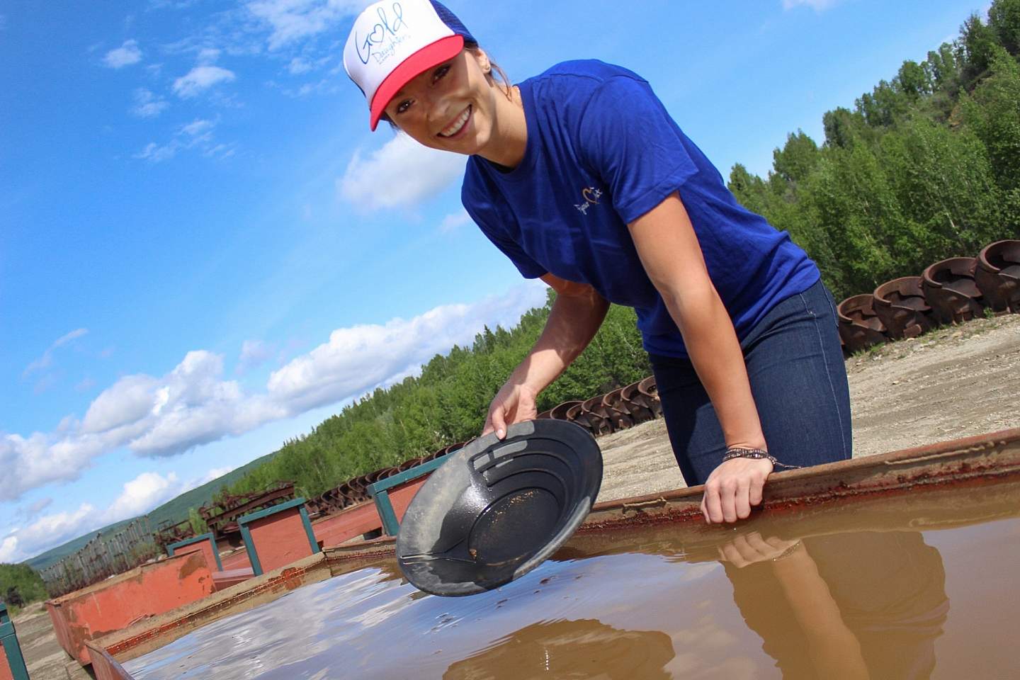 A smiling woman pans for gold outside.
