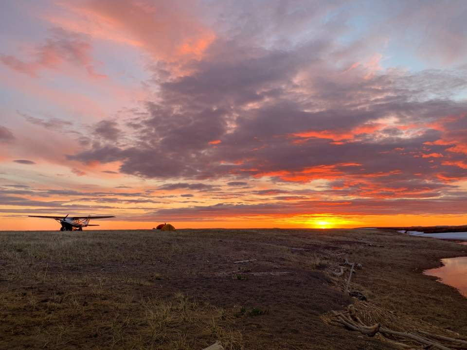 A landed bush plane sits in front of a stunning golden sunset.