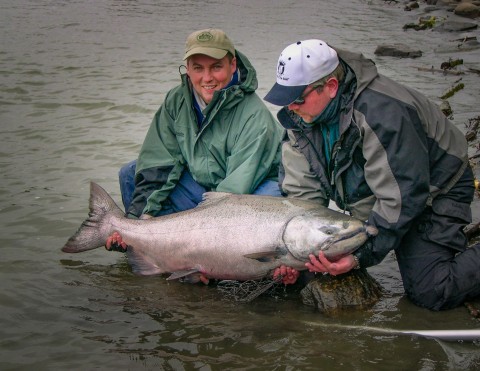 Two people kneel in the water to hold a large fish they caught.