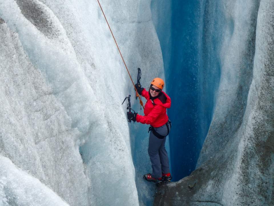 Woman in a red coat ice climbing on Root Glacier.