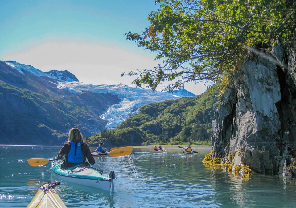 People kayaking in the Prince William Sound with a glacier in the back ground.