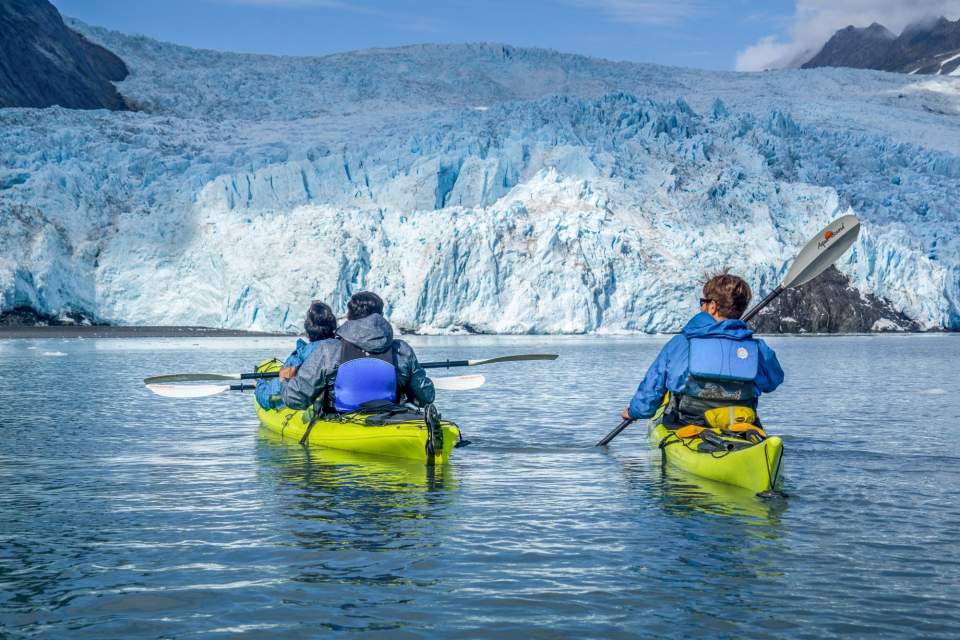 People kayaking on icy blue waters next to a glacier.
