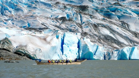 People row a canoe through the water towards a glacier.