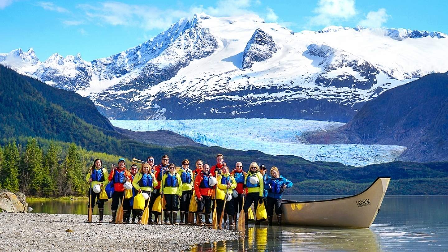 People row a canoe through the water towards a glacier.