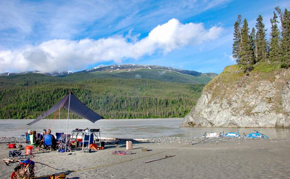 A campsite set up on the beach of an Alaskan river on a summer day.