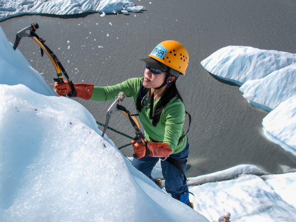 A woman ice climbs up the side of a glacier.