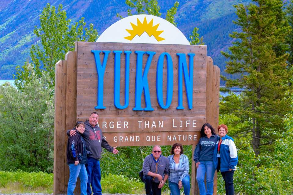 A group poses in front of a large sign that says "Yukon".