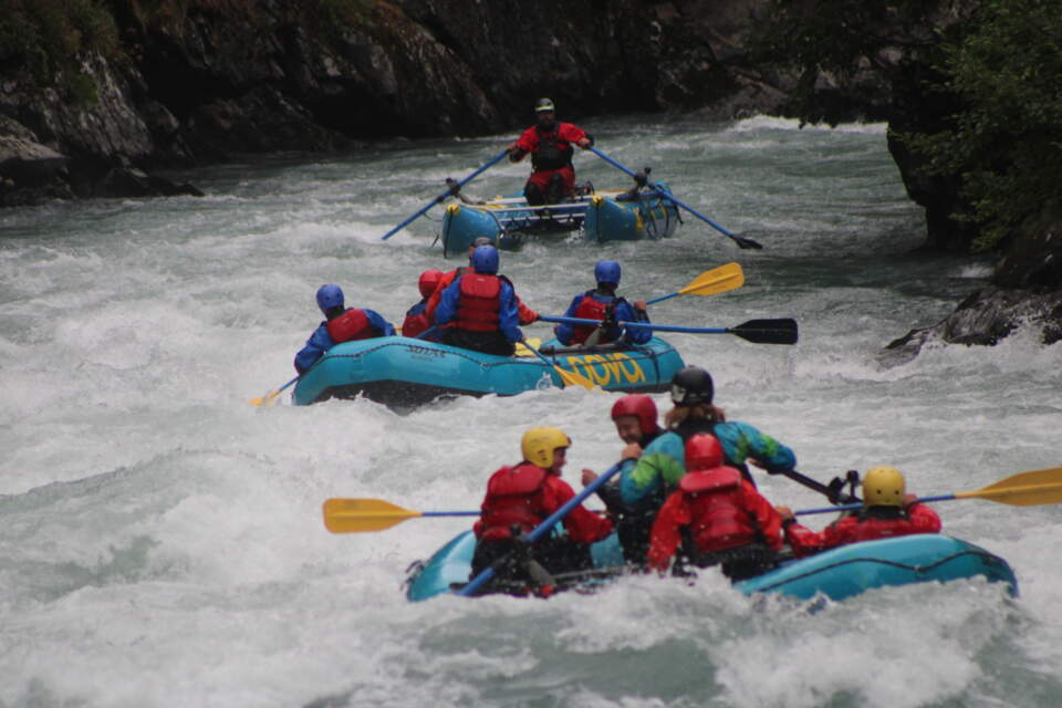 People in an inflatable raft race down a whitewater river.