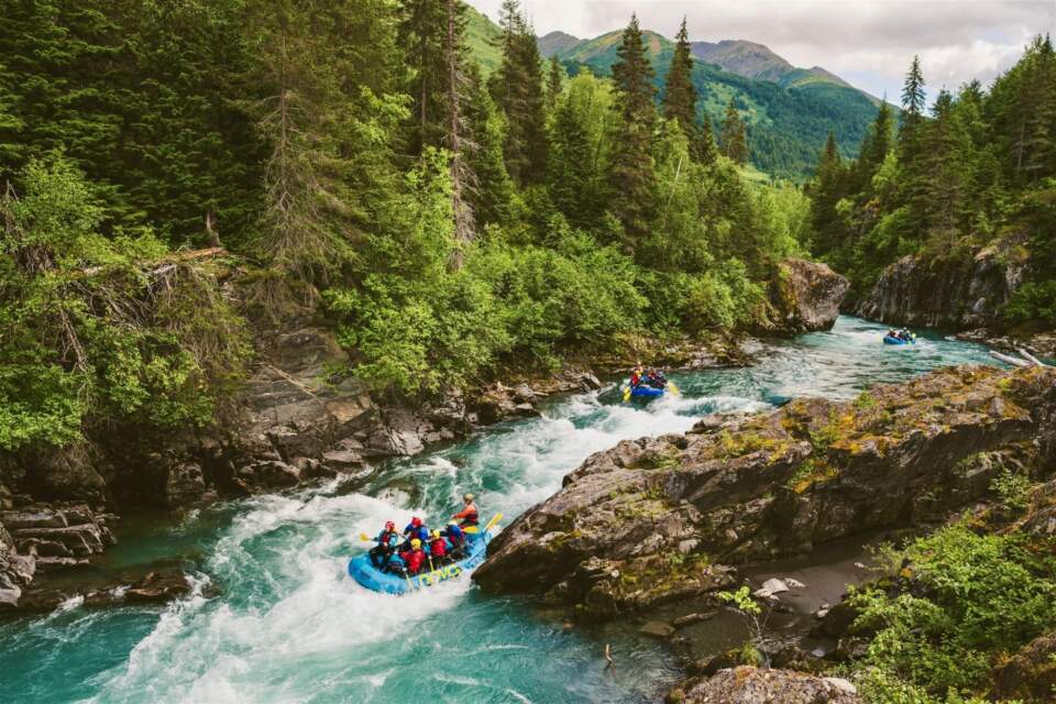 People in an inflatable raft race down a whitewater river.