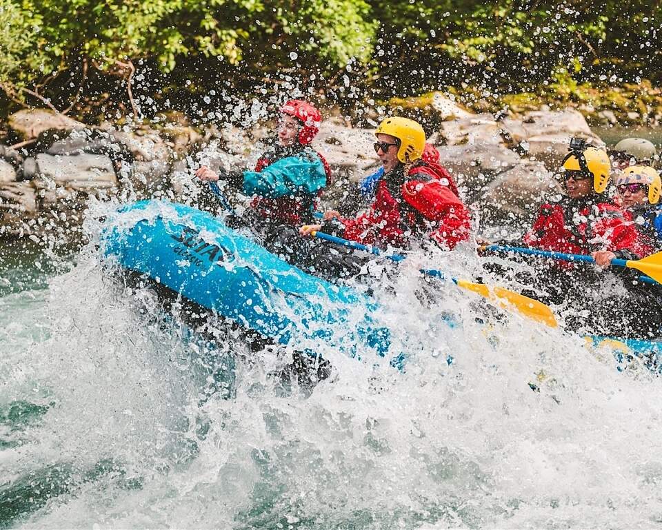 People in an inflatable raft race down a whitewater river.