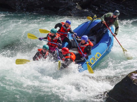People in an inflatable raft race down a whitewater river.