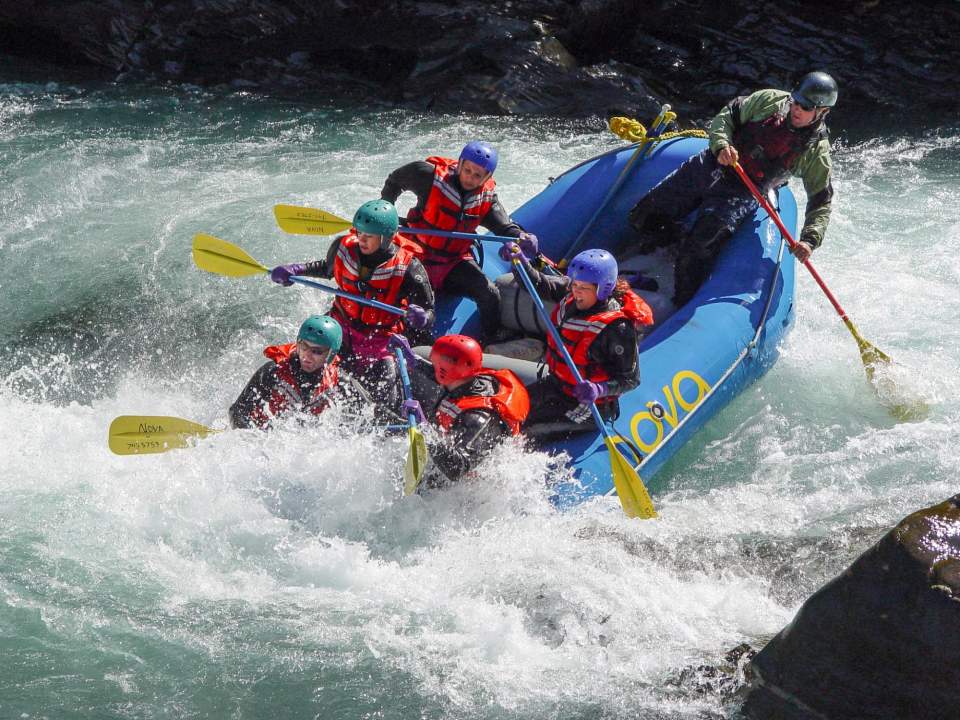 People in an inflatable raft race down a whitewater river.