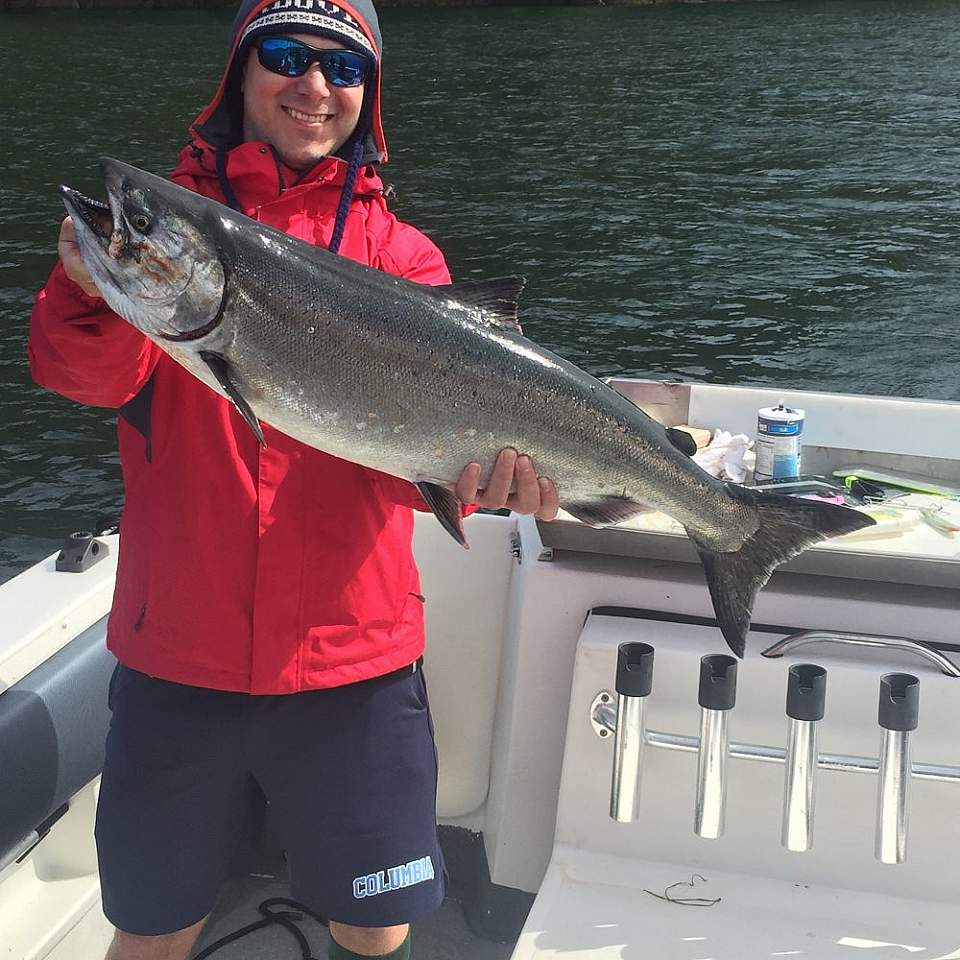 A man in a red jacket in a boat holds a large fish.